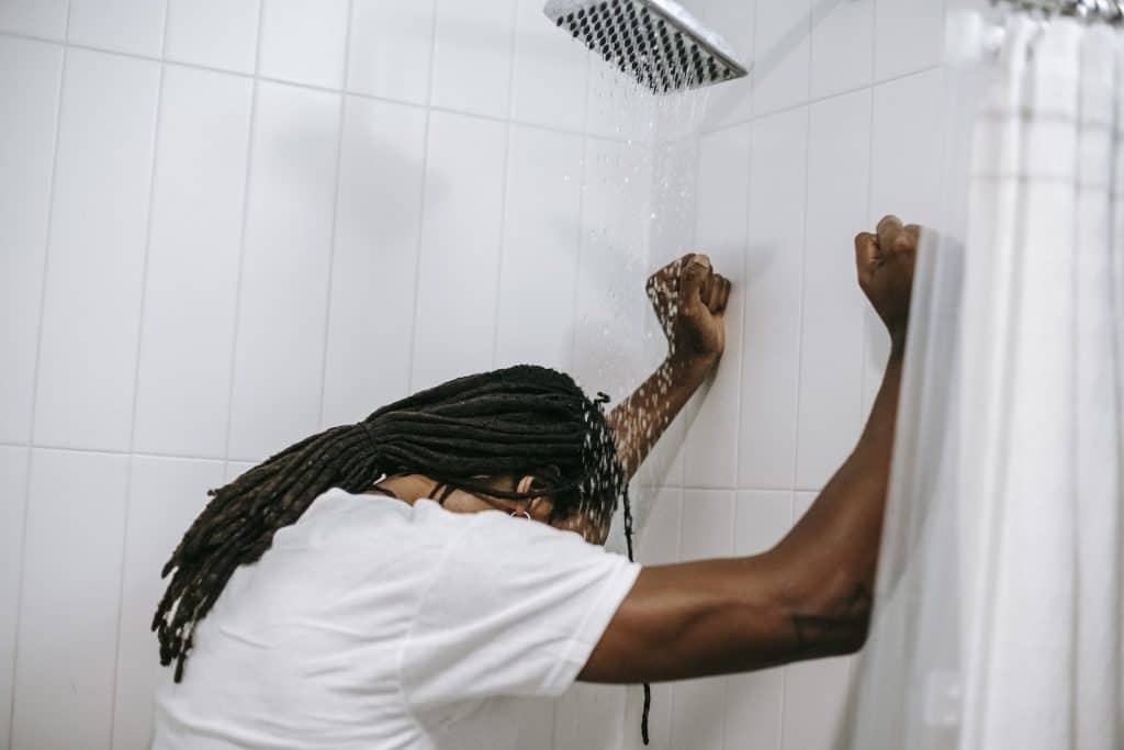 Unrecognizable depressed black man under water flow in shower