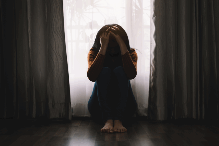 Woman sitting in the dark holding her head, showing signs of depression.
