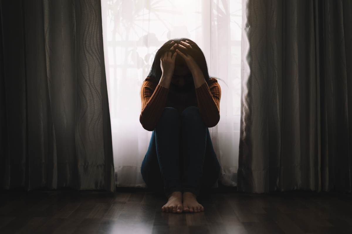 Woman sitting in the dark holding her head, showing signs of depression.