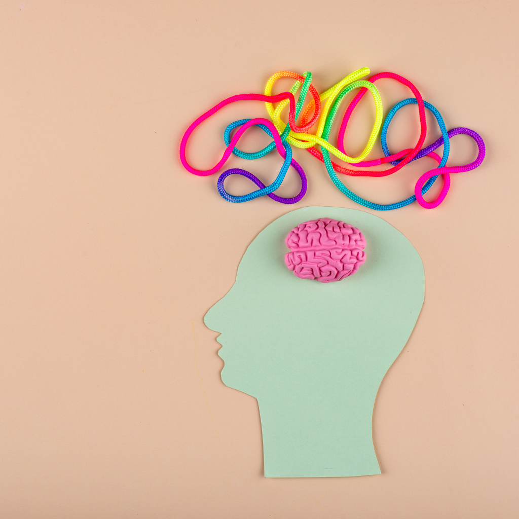OCD vs. ADHD: Intersection of Symptoms and Strategies 2 Paper cutout of a human head with a brain and tangled colorful cords above it, symbolizing neurodivergent thinking and cognitive complexity.