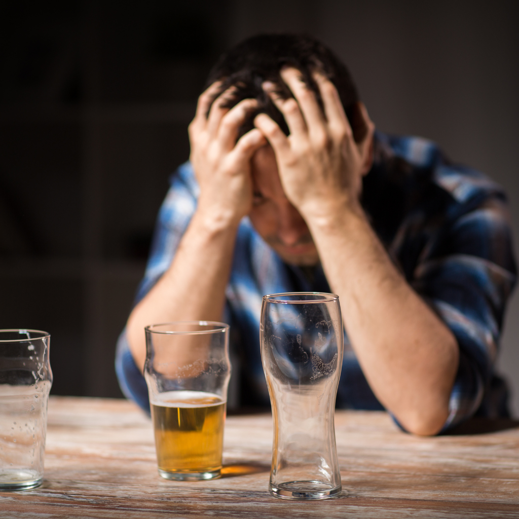 Exploring the Intersection of Masculinity and Men's Mental Health 2 Man sitting with head in hands and empty beer glasses, showing emotional distress and alcohol struggle.