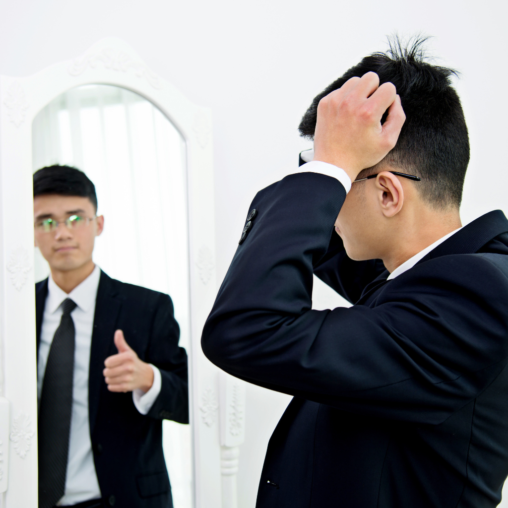 Work-Life Harmony: Navigating Bipolar Disorder in the Workplace 1 Man adjusting his appearance in the mirror while his reflection gives a thumbs up, symbolizing the dual challenges and efforts to maintain confidence at work with bipolar disorder.