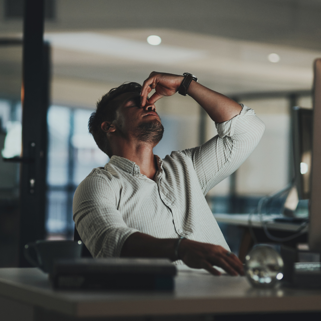 Work-Life Harmony: Navigating Bipolar Disorder in the Workplace 2 Frustrated man sitting at his desk with his hand on his face, capturing the struggle of managing work-related stress and focus while living with bipolar disorder.