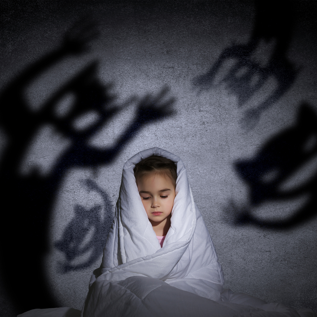 The Role of Parenting in Addressing Fears and Phobias in Children 1 Child wrapped in a blanket with shadowy monsters on the wall, representing childhood fears and phobias.