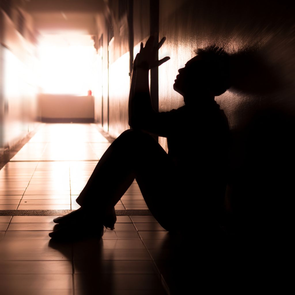 Person sitting in shadowed hallway, reflecting deep sadness and emotional overwhelm.