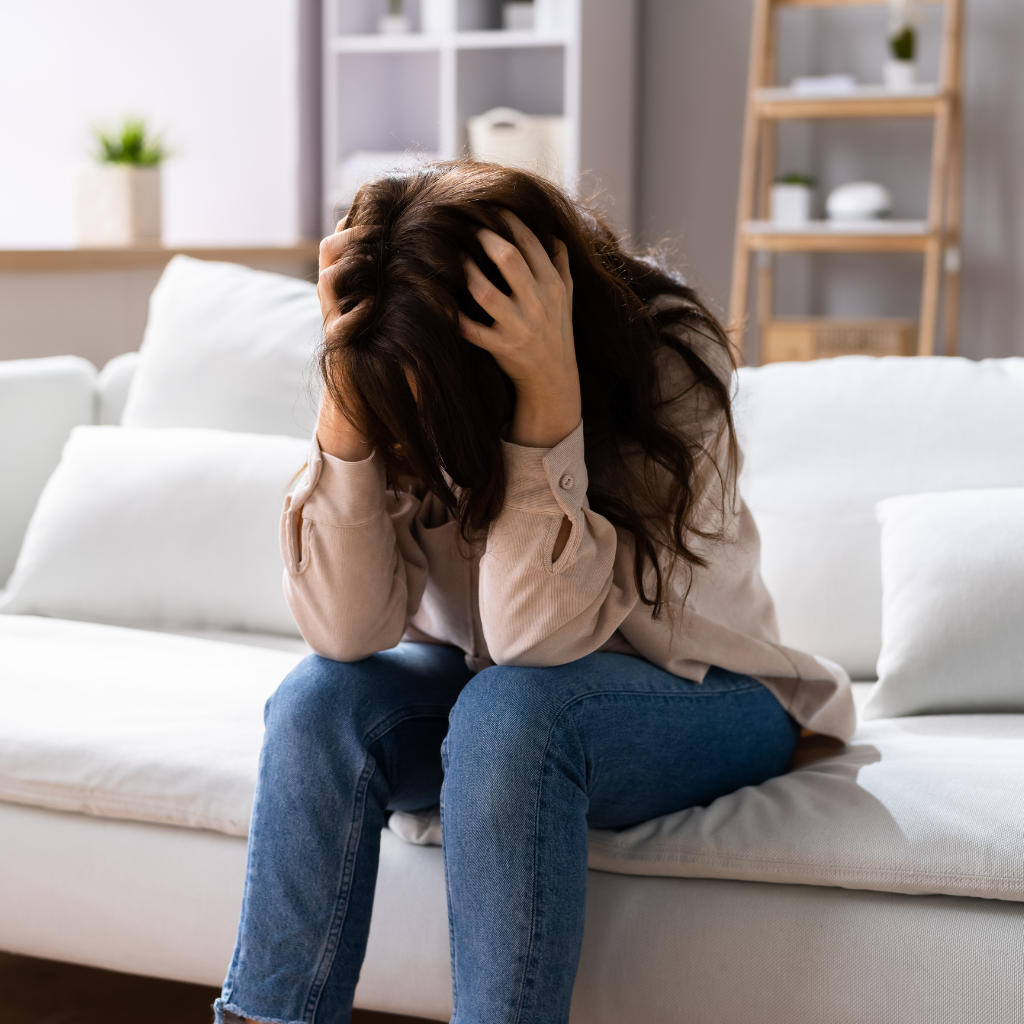 What Is Chronic Impulsivity? Understanding Impulse-Control Disorders 1 Woman sitting on a couch, stressed and overwhelmed by guilt after impulsive behavior.