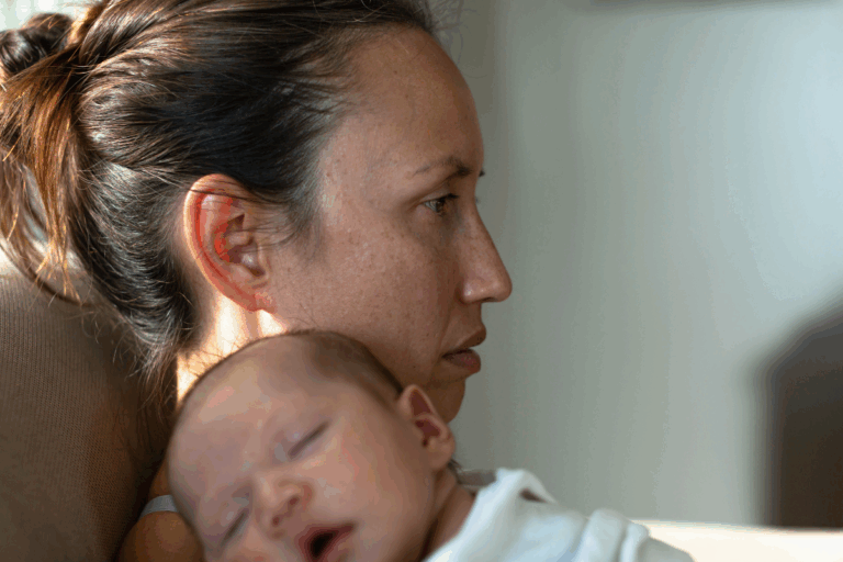 New mom holding her baby, looking distant and emotionally drained, showing signs of postpartum depression.