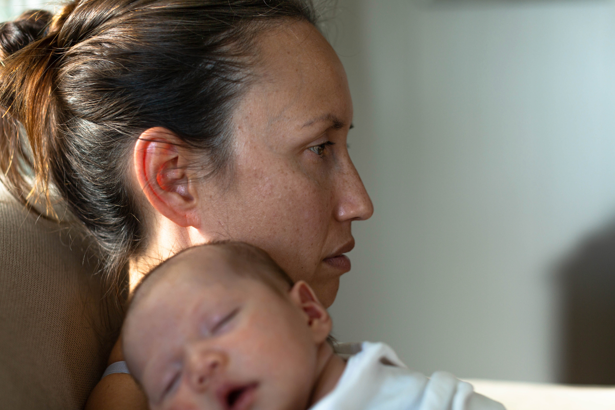 New mom holding her baby, looking distant and emotionally drained, showing signs of postpartum depression.
