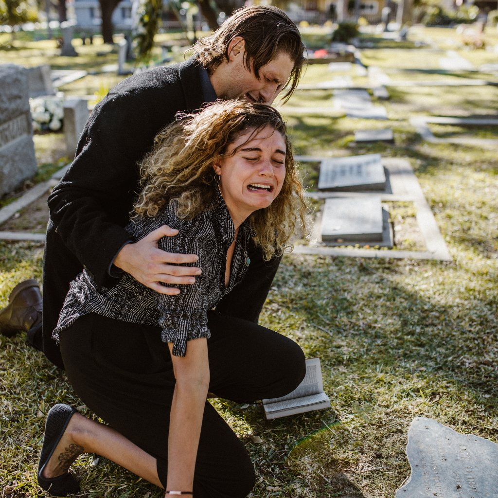 Grieving couple mourning at a cemetery after a significant loss.