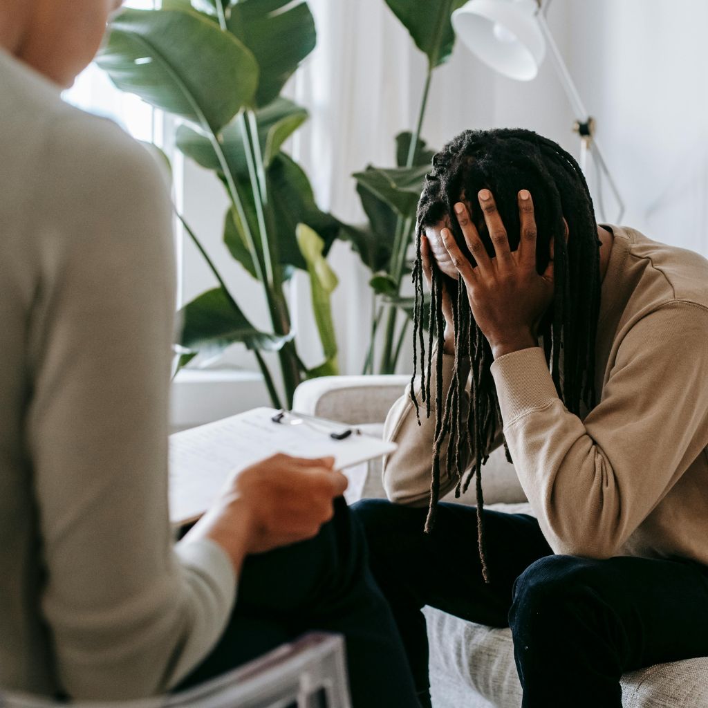Imposter Syndrome and Mental Health: The Hidden Cost of Self-Doubt 2 Man holding his head in his hands while talking to a therapist, showing the emotional weight of imposter syndrome.