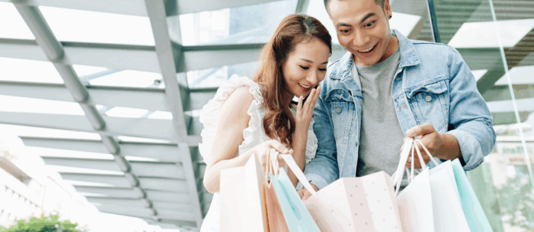 Couple excitedly looking at shopping bags, symbolizing impulsive spending.