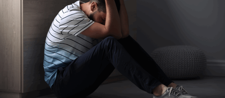 Man sitting on the floor with head in arms, illustrating the emotional pain of rejection sensitive dysphoria.