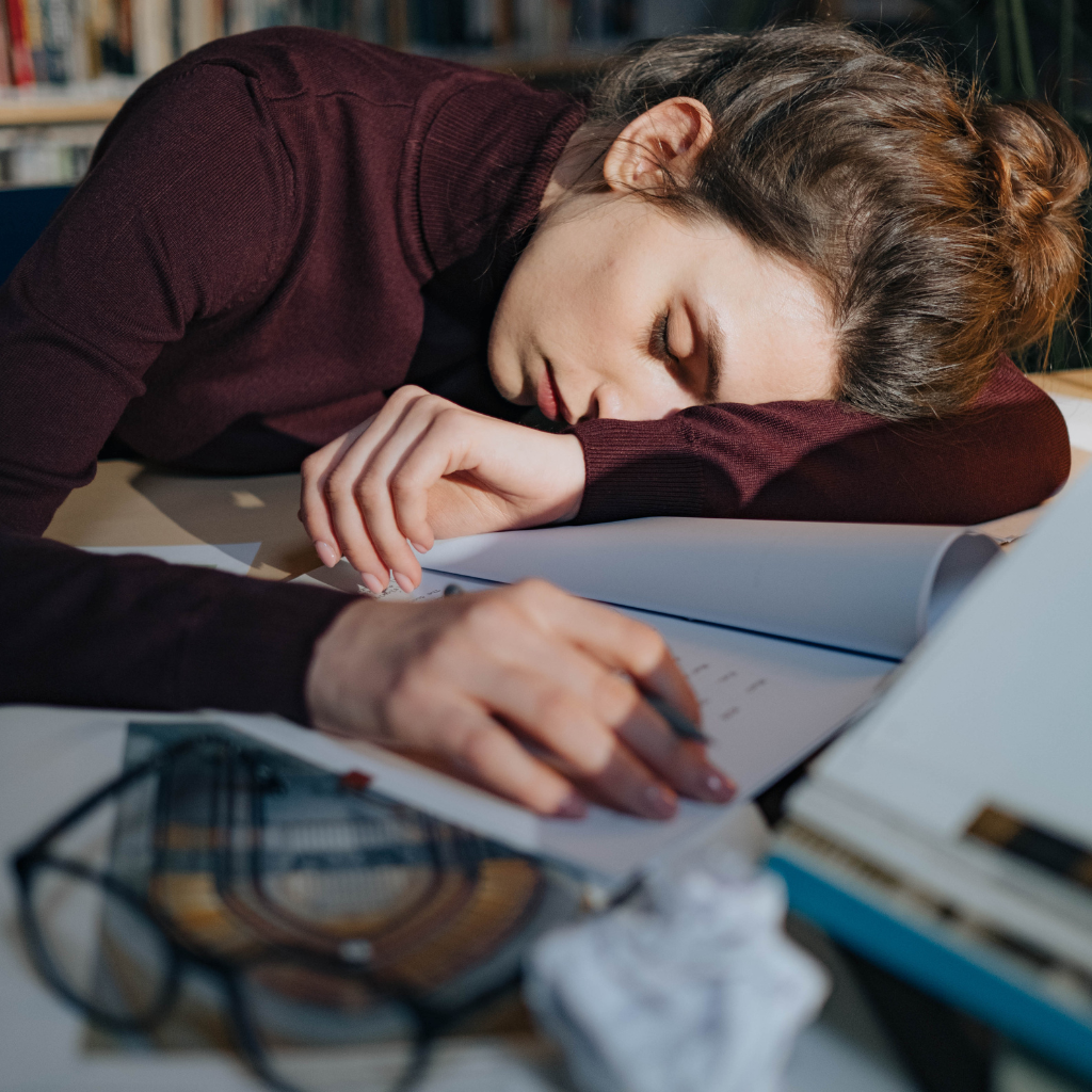 Woman exhausted and resting on desk, showing fatigue and low energy, common symptoms of persistent depressive disorder (PDD).