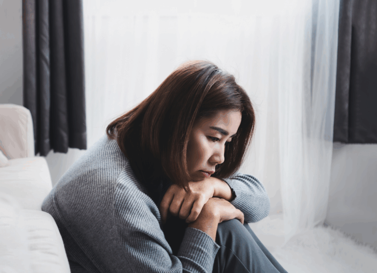 Woman sitting on the floor with her arms wrapped around her knees, appearing sad and depressed