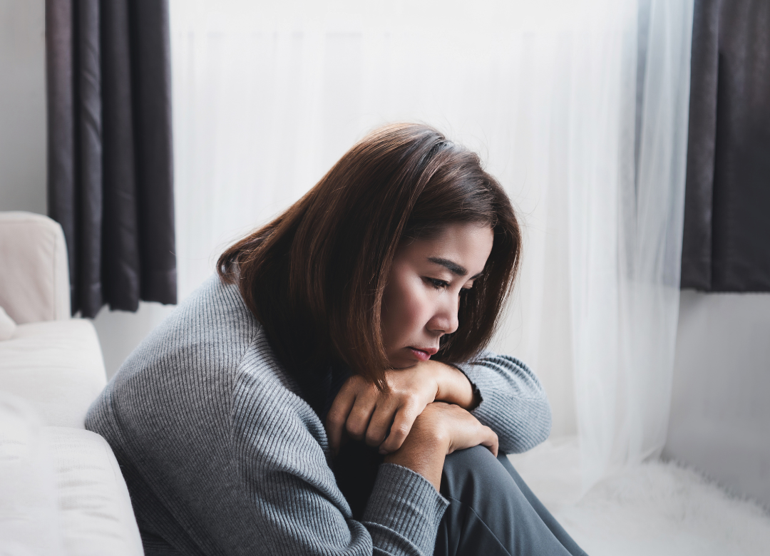 Woman sitting on the floor with her arms wrapped around her knees, appearing sad and depressed