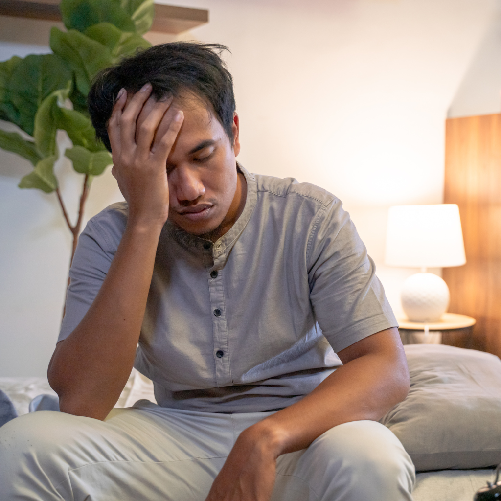 The Intersection Of ADHD and Sleep: Why Insomnia Or Restless Sleep Often Co-Occurs 1 Man sitting on a bed looking exhausted and rubbing his head, illustrating the daytime fatigue and frustration linked to sleep problems in ADHD.