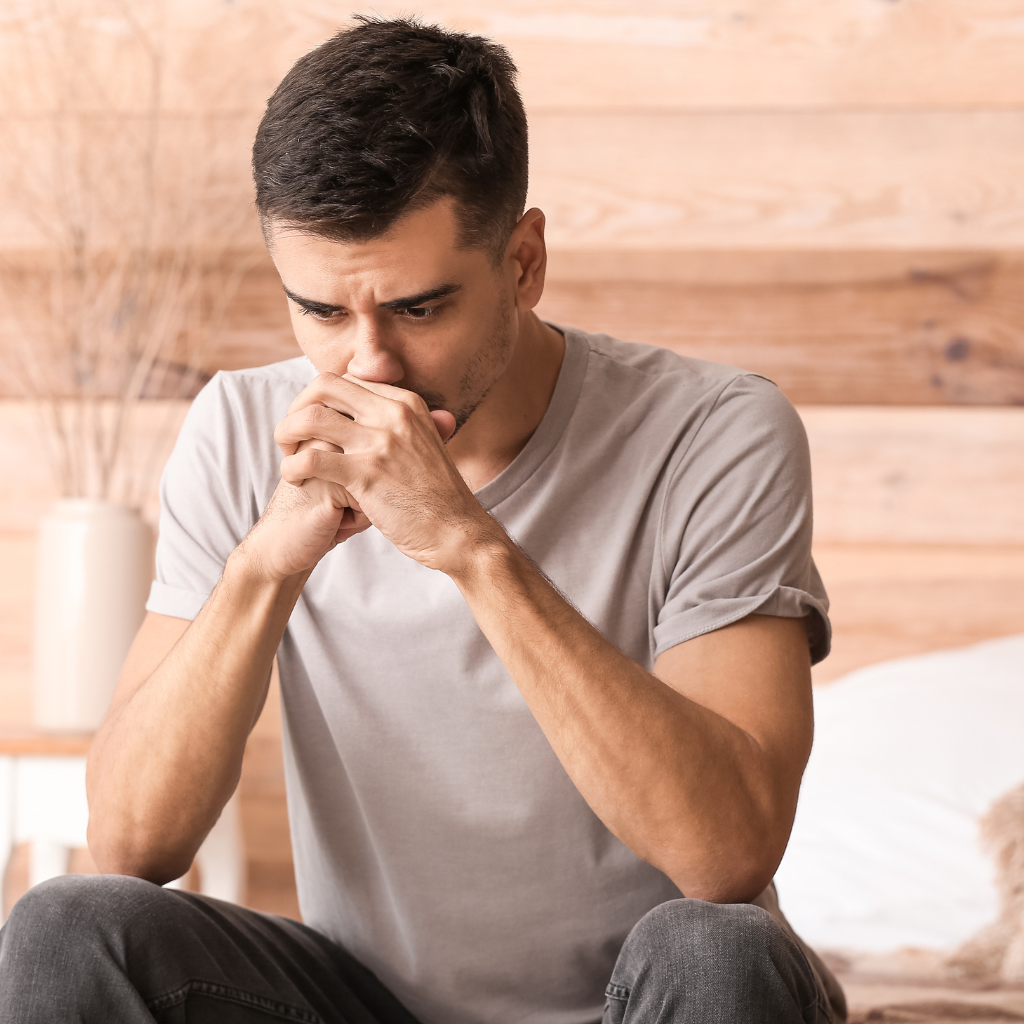 Man sitting with clasped hands, looking distressed.