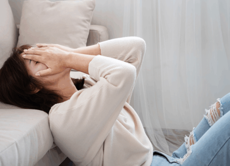Animo Sano Psychiatry 35 Woman sitting on the floor with her hands covering her face, showing overwhelm related to ADHD and anxiety.