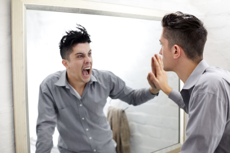 Man looking in the mirror and seeing himself yelling back, representing intense mood changes.