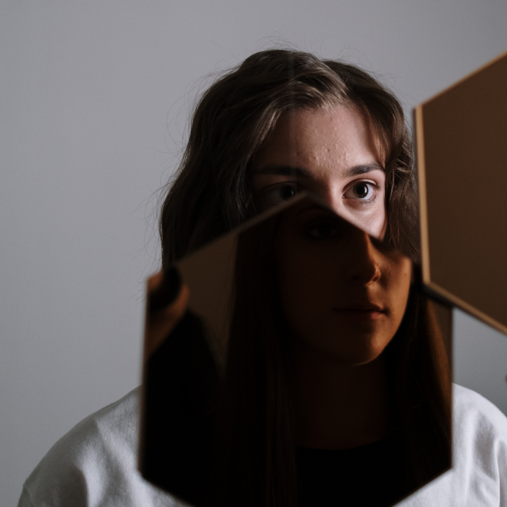 Woman looking at her reflection through broken mirror pieces, showing how bipolar experiences can feel divided.