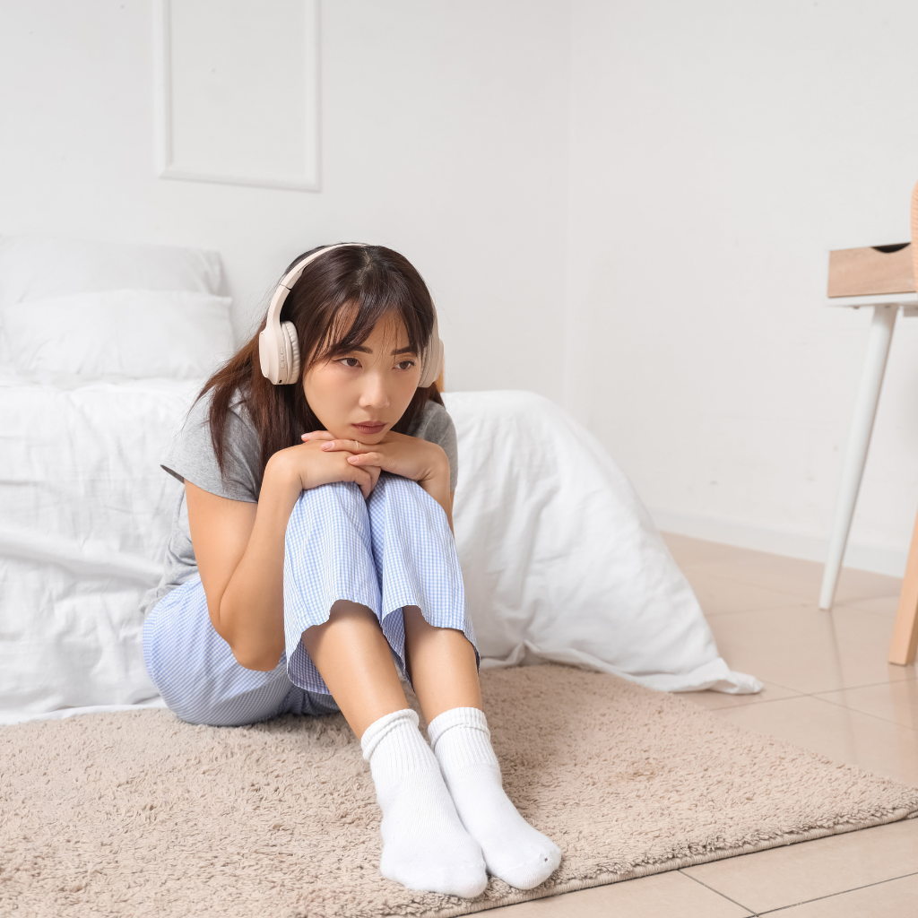 Woman sitting on the floor with headphones, looking sad and withdrawn.