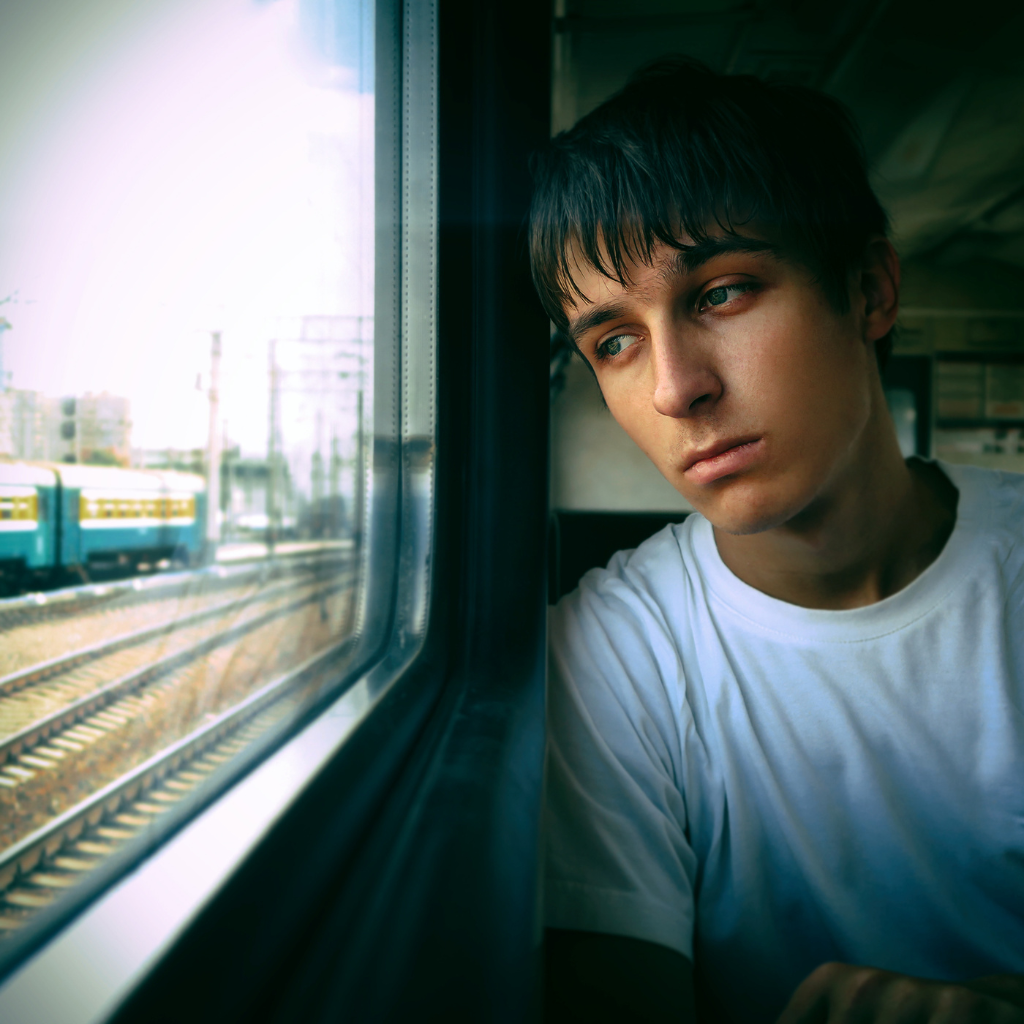 A person looking out a train window, appearing tired and deep in thought.