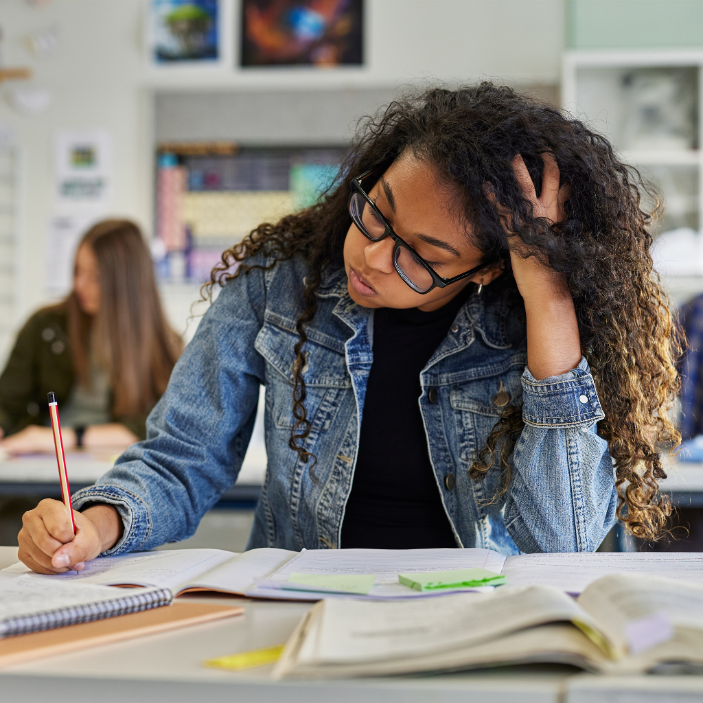 A student studying at a desk, appearing distracted and overwhelmed while trying to focus.