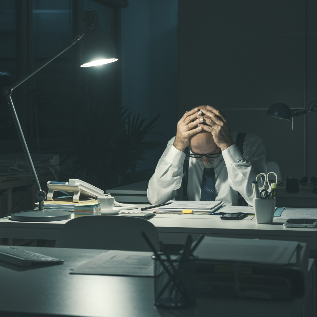 Employee experiencing work anxiety while overwhelmed by deadlines and paperwork at his desk