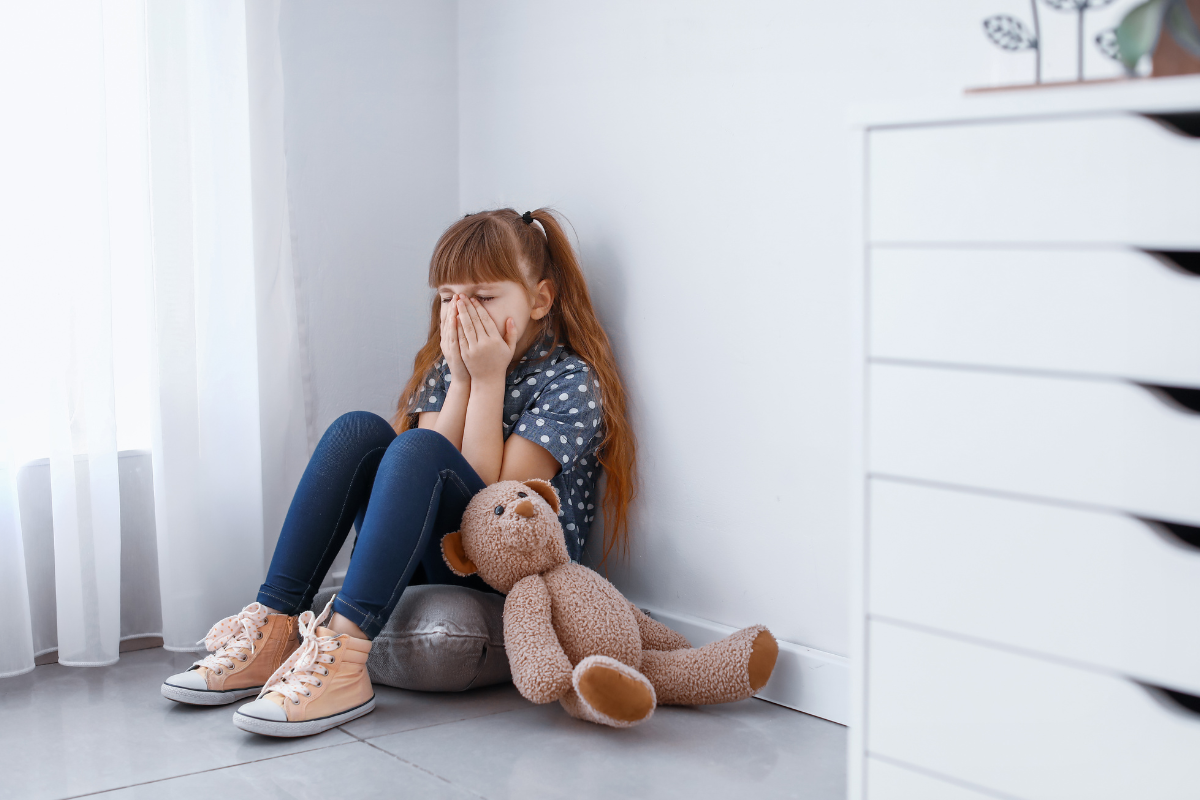 Young child showing signs of panic attack, sitting alone and covering her face