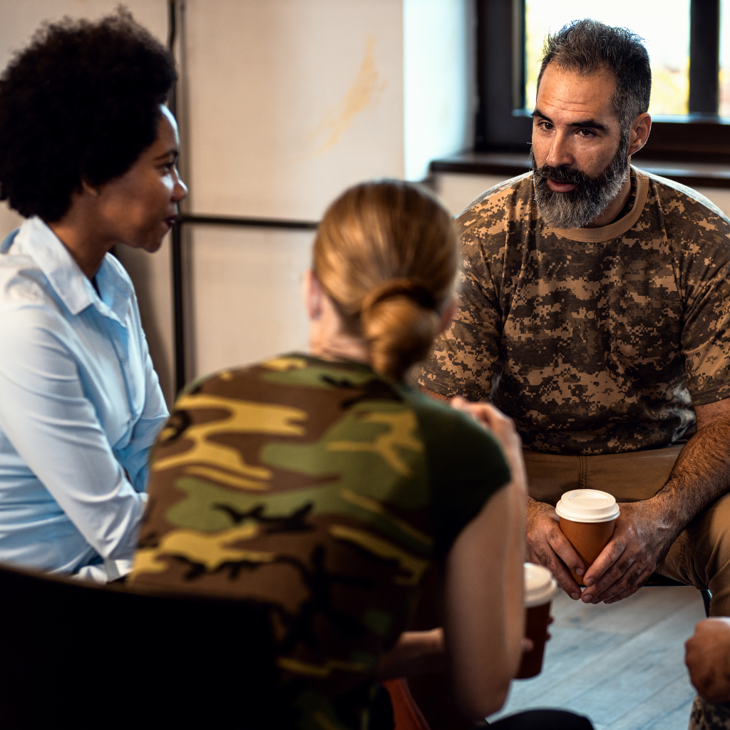 Veterans sitting together in a therapy session, discussing trauma and recovery.