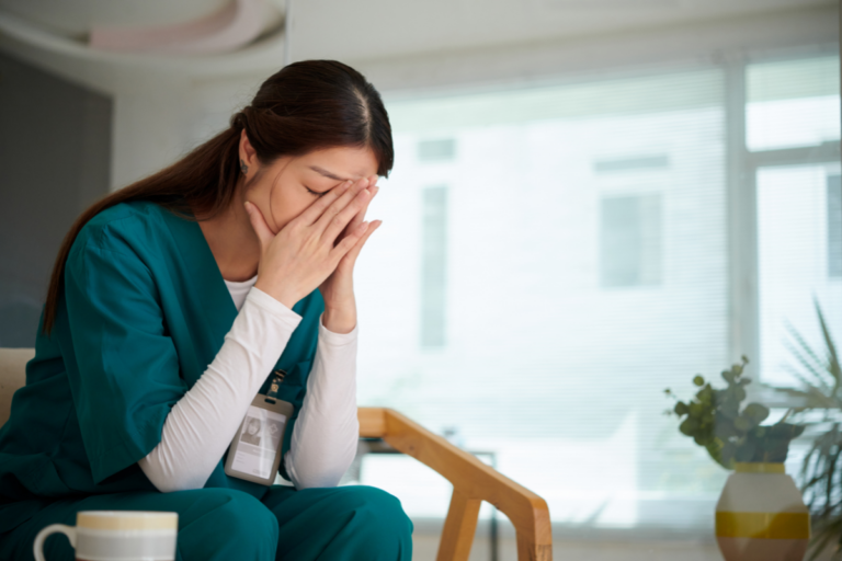 Healthcare worker sitting with head in hands, illustrating emotional strain related to secondary traumatic stress.