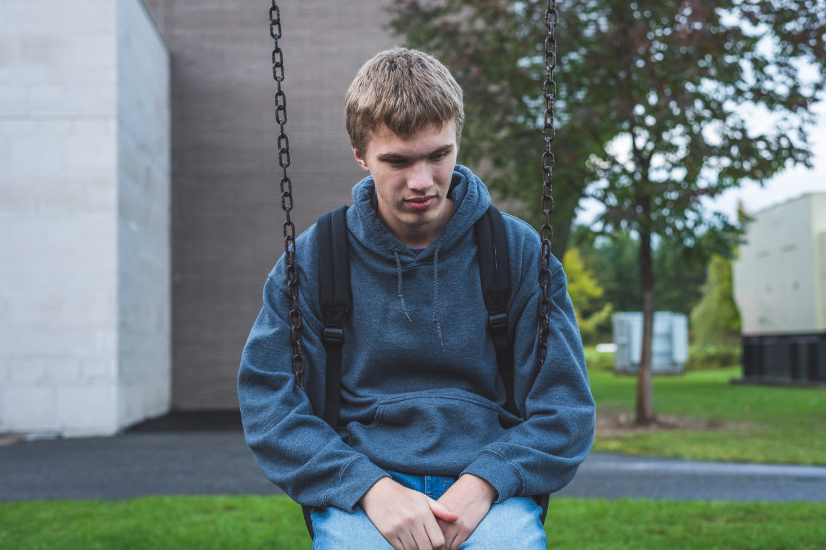 Teen boy sitting alone on a swing with signs of emotional distress.
