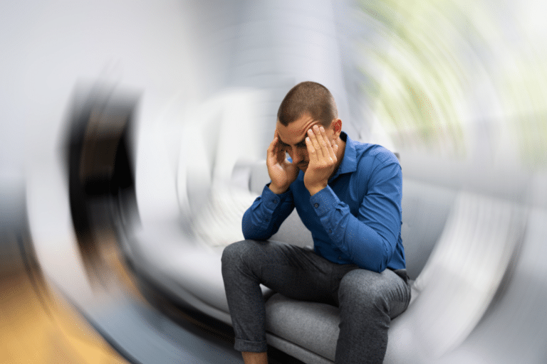Man sitting on a couch holding his head with blurred surroundings, representing brain fog and difficulty concentrating