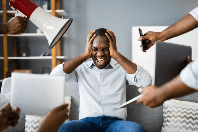 Man overwhelmed by sensory overload from noise, screens, and competing demands.