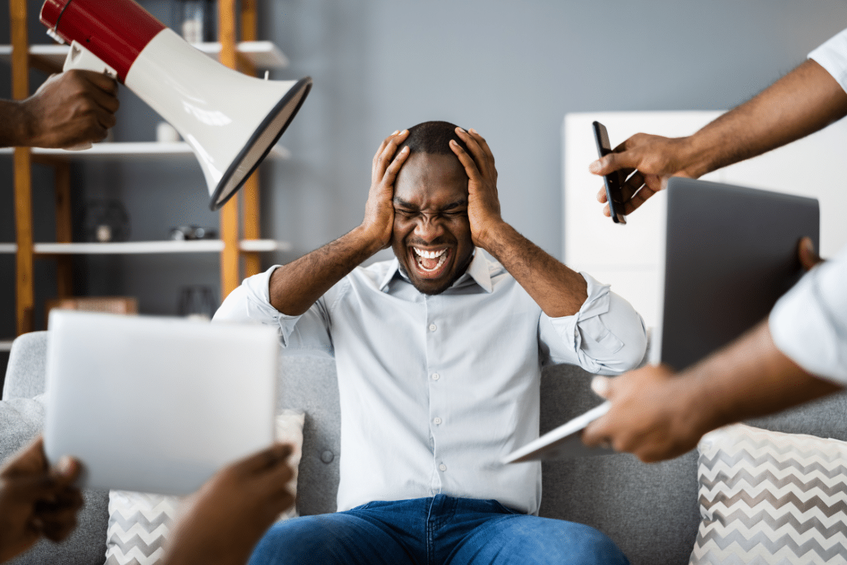 Man overwhelmed by sensory overload from noise, screens, and competing demands.