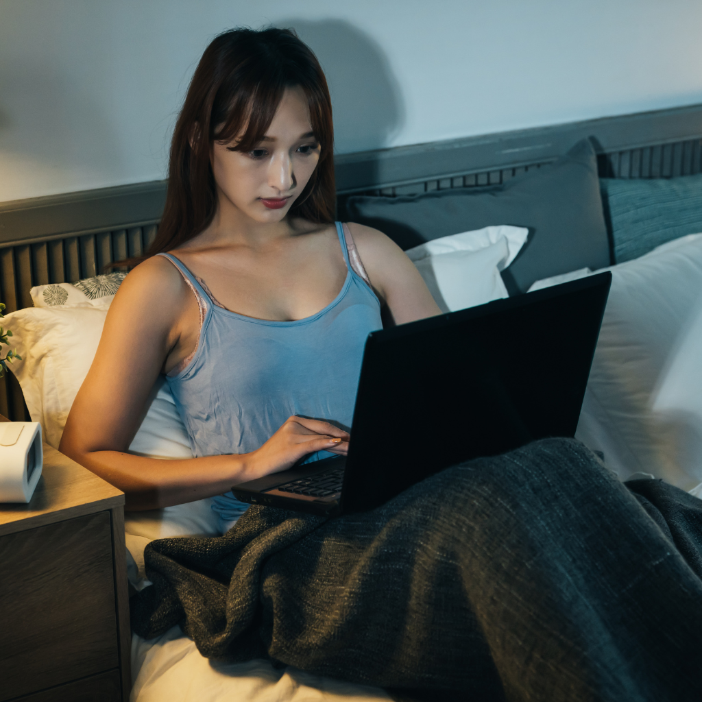 What Is Revenge Sleep Procrastination? Why You Stay Up Even When You're Exhausted 1 Woman using a laptop in bed late at night to reclaim personal time.