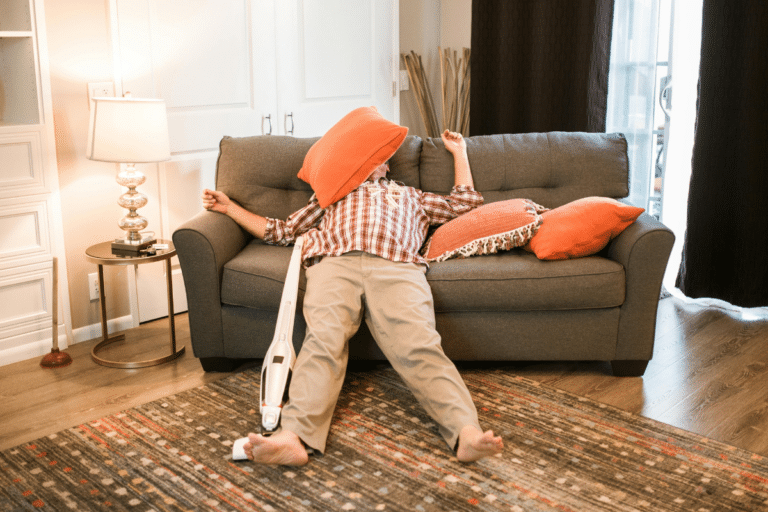 Person lying on a couch beside a vacuum cleaner, illustrating ADHD paralysis and difficulty starting tasks.