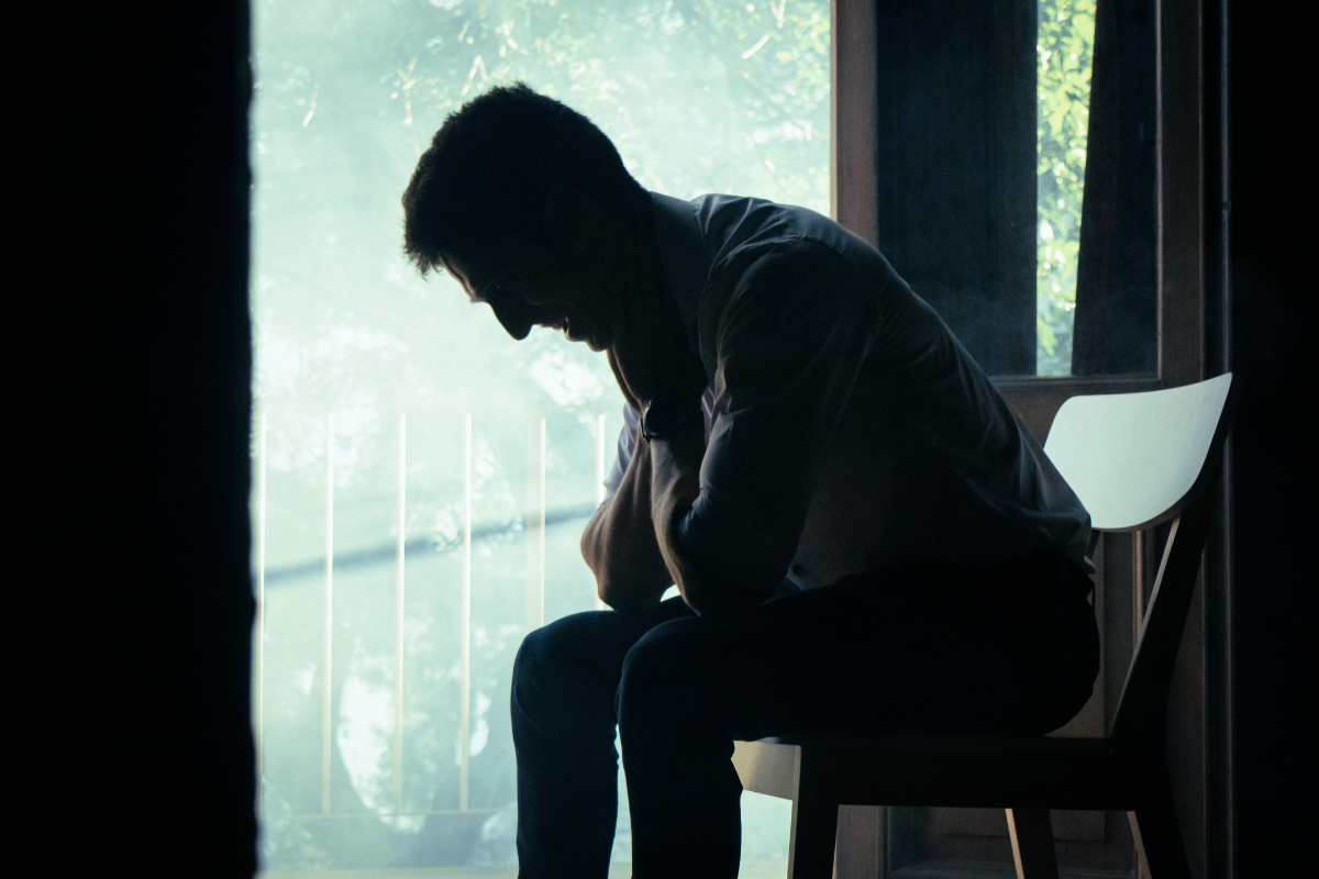 Man sitting alone with his head down, appearing distressed and overwhelmed by intrusive thoughts associated with harm OCD.