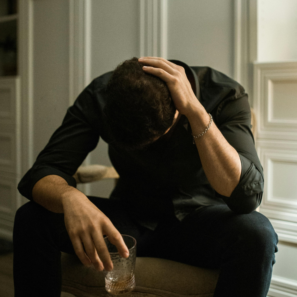 Men's Midlife Crisis: When Everyday Pressure Becomes Something More 1 Man sitting with his head down and holding a glass while experiencing emotional distress and mental health challenges during midlife.