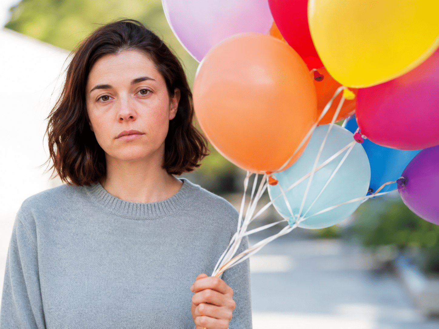 woman holding balloons for a birthday party with blank expression and feels nothing