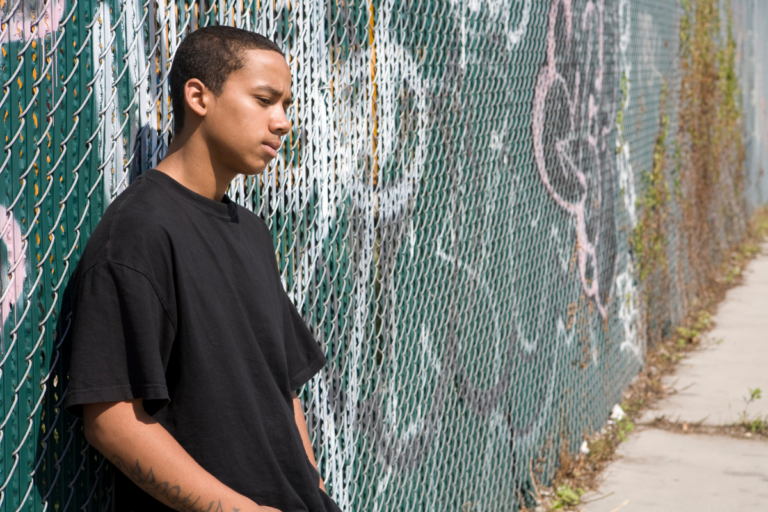 Teen boy standing alone by a chain-link fence, reflecting teen depression signs parents may mistake for moodiness.