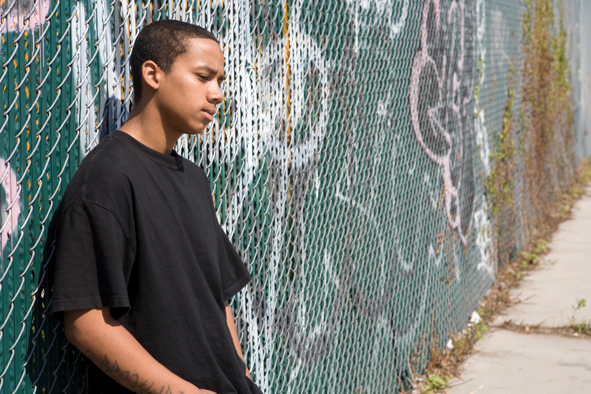 Teen boy standing alone by a chain-link fence, reflecting teen depression signs parents may mistake for moodiness.