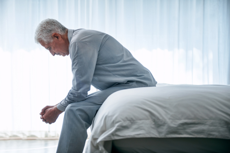 Older man sitting alone on the edge of a bed, showing how late-life depression can look in older adults.