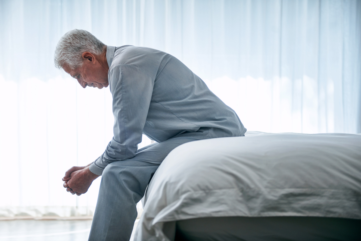 Older man sitting alone on the edge of a bed, showing how late-life depression can look in older adults.