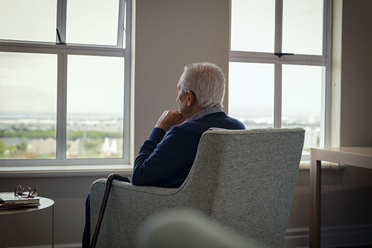 Older man sitting alone by a window, reflecting loneliness and isolation in older adults.