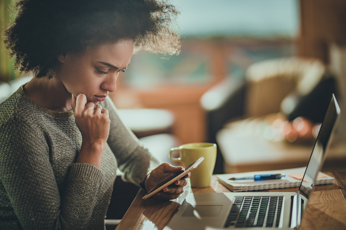Woman looking concerned while using her phone and laptop, reflecting health anxiety from googling symptoms online.