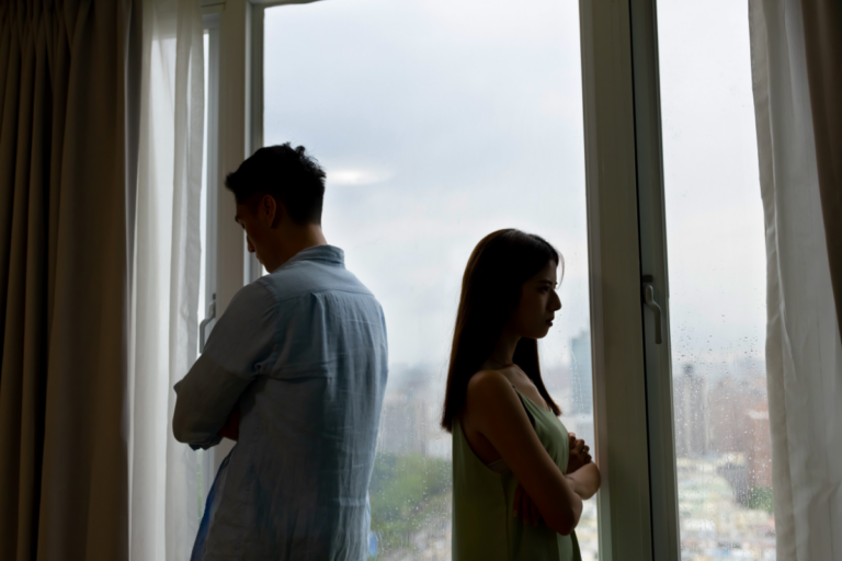 Couple standing apart with crossed arms, showing emotional distance in a strained relationship.