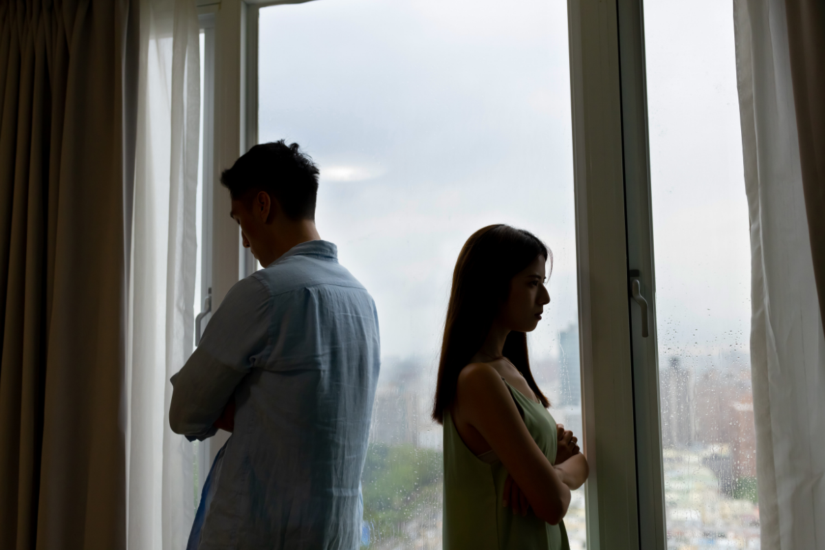 Couple standing apart with crossed arms, showing emotional distance in a strained relationship.