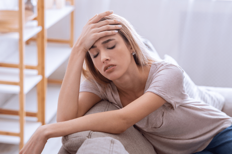 Woman resting on a couch with her hand on her forehead, reflecting PMDD symptoms like fatigue and emotional distress.