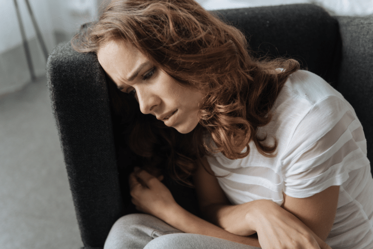 Woman leaning against a couch looking distressed, reflecting mood changes linked to bipolar disorder and hormones in women.